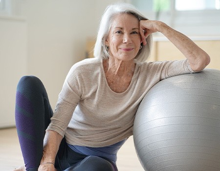 Senior woman smiling while resting against balance ball