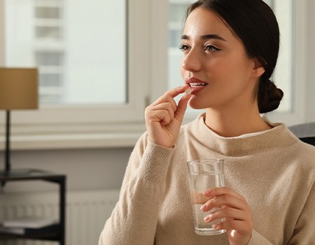 a woman holding up a pill to her lips and holding a glass of water