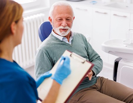 a dentist holding a clipboard and talking to a patient