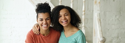 Two young women smiling next to white staircase
