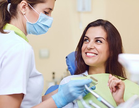 Woman in dental chair smiling at dentist in blue gloves and mask