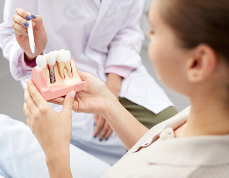 A dentist pointing at a dental implant model while consulting with a patient