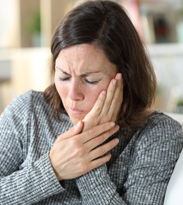 Woman in a grey sweater on the couch with toothache