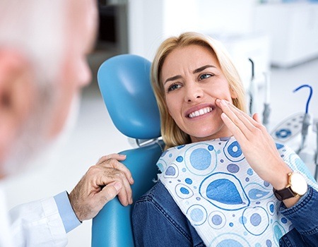 Woman in dental chair holding cheek in pain