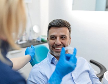 Male patient smiling at dental assistant holding Invisalign aligner