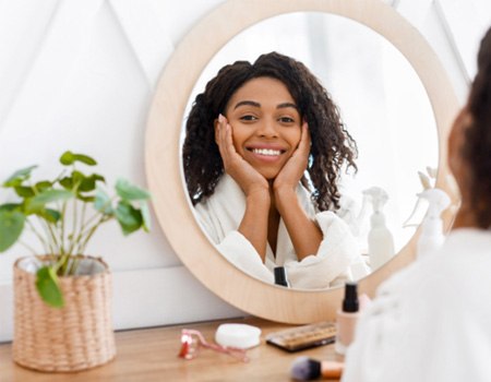 Woman in white robe smiling at reflection in mirror