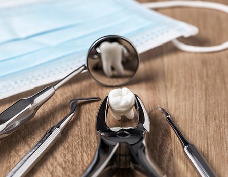 Dental forceps holding a tooth next to other dental tools