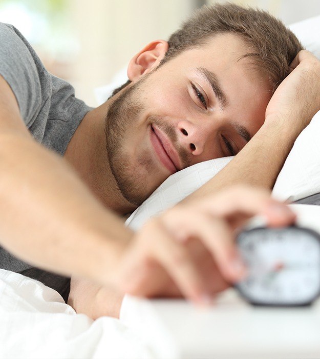 Smiling man turning off alarm clock