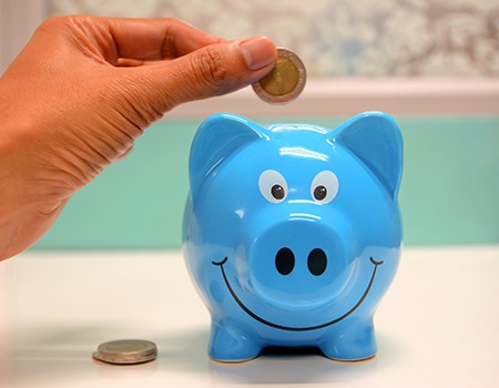 Hand putting coin in blue piggy bank