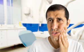 Distressed man holding his cheek in pain before seeing an emergency dentist