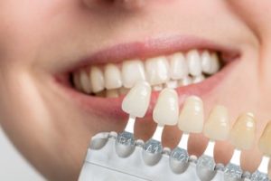 A woman smiling as the dentist holds a dental color scale to her teeth