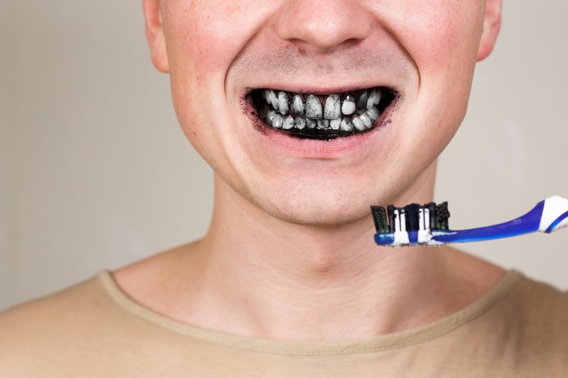man brushing teeth with charcoal toothpaste
