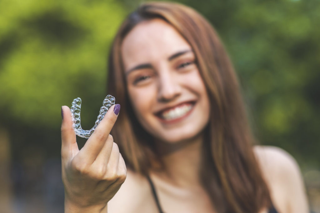 smiling person holding an Invisalign aligner tray