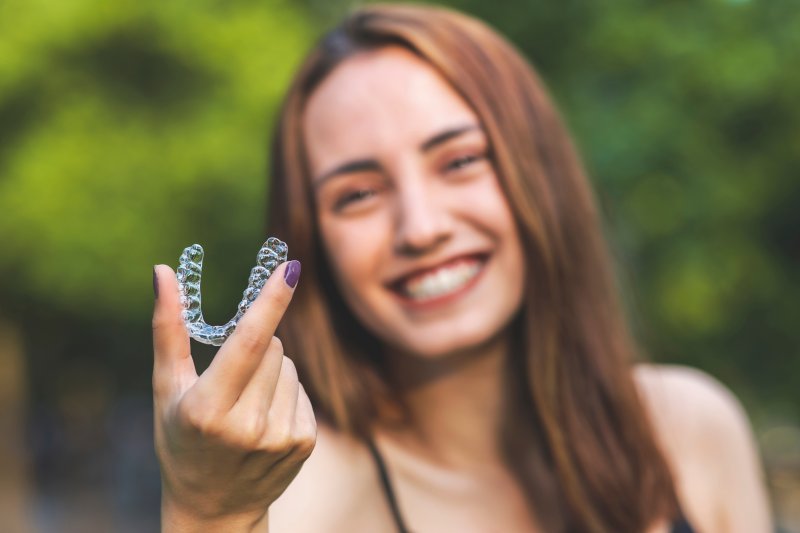 Young woman holding her Invisalign aligner and smiling