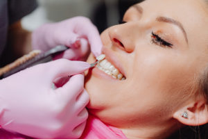 Gloved hands holding veneer next to woman’s tooth