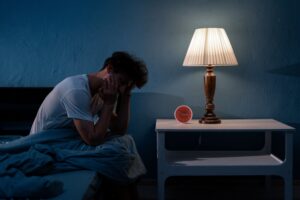 Man sitting up in bed with clock and lamp on bedside table
